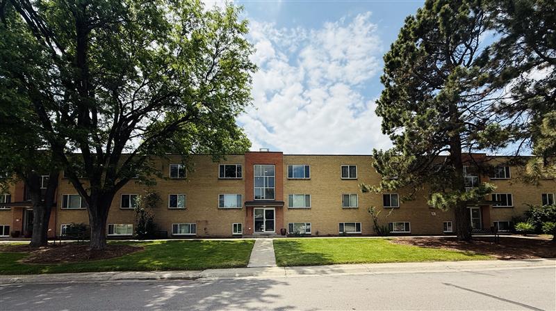 Charming apartment building surrounded by lush trees and well-maintained green lawn, offering a serene and inviting atmosphere.