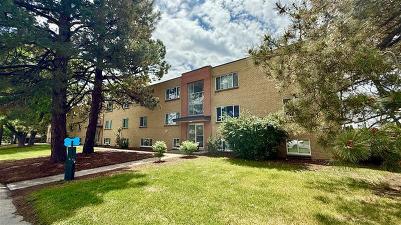 Charming brick apartment building with lush greenery and a spacious lawn, offering a serene residential ambiance.