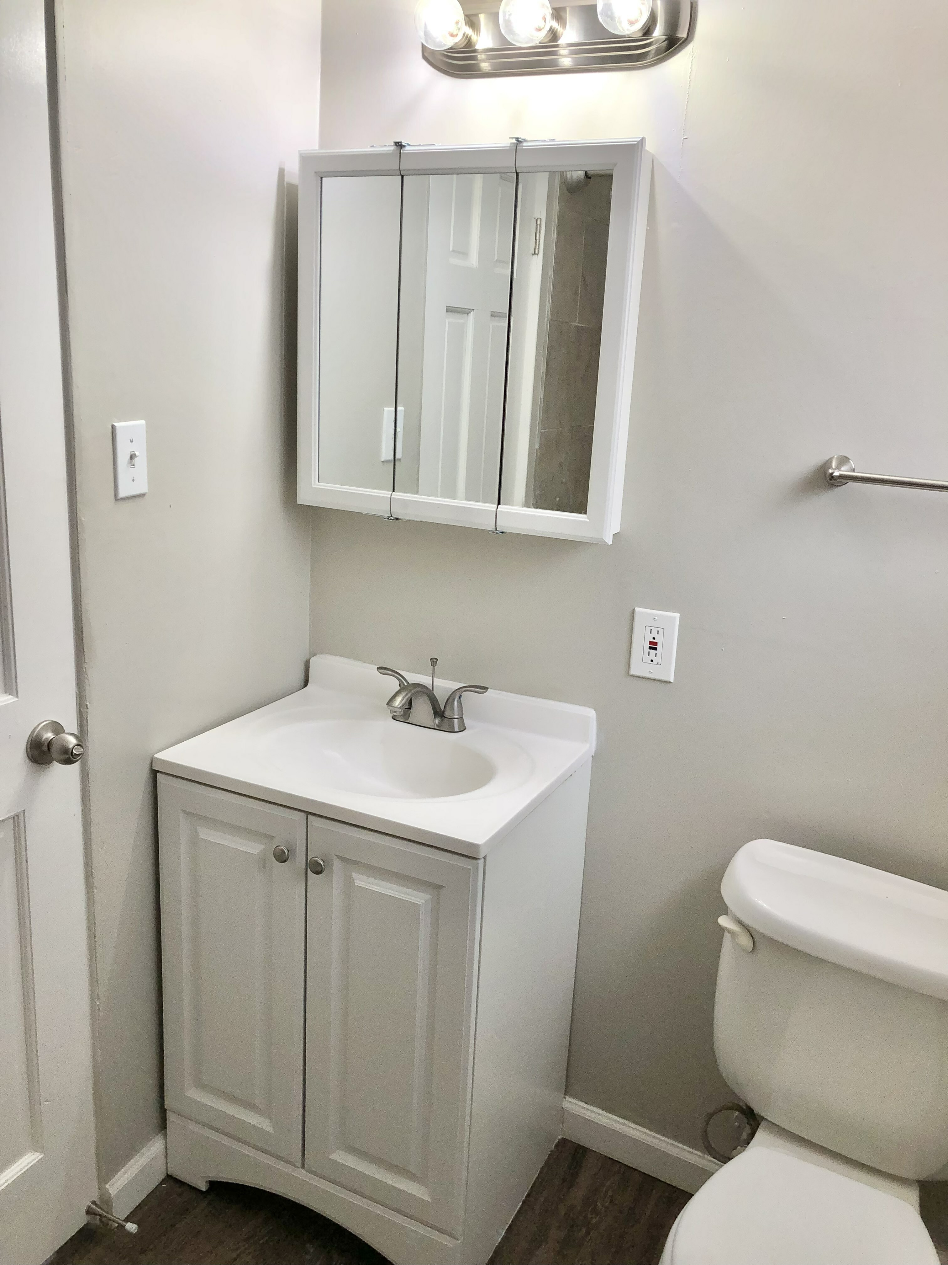 Modern bathroom with sleek white vanity, mirrored cabinet, and bright lighting.