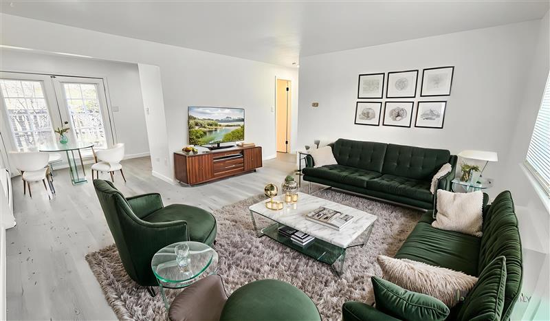 Bright and modern living room with elegant green furniture, cozy shaggy rug, and a wall-mounted TV, connected to a dining area with natural light streaming through large windows.