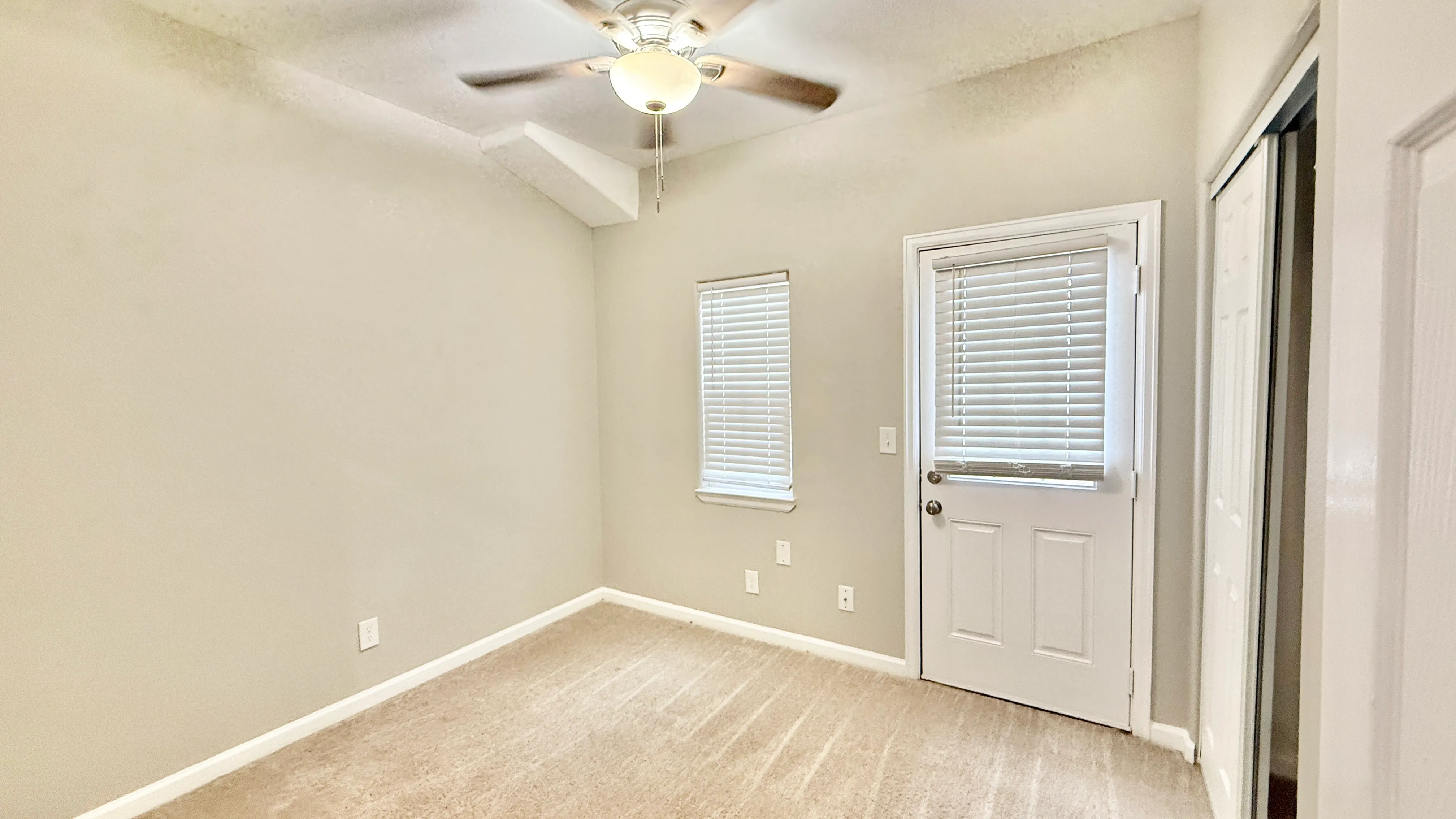 Bright bedroom with soft carpet, dual windows, and ceiling fan, providing comfort and style.