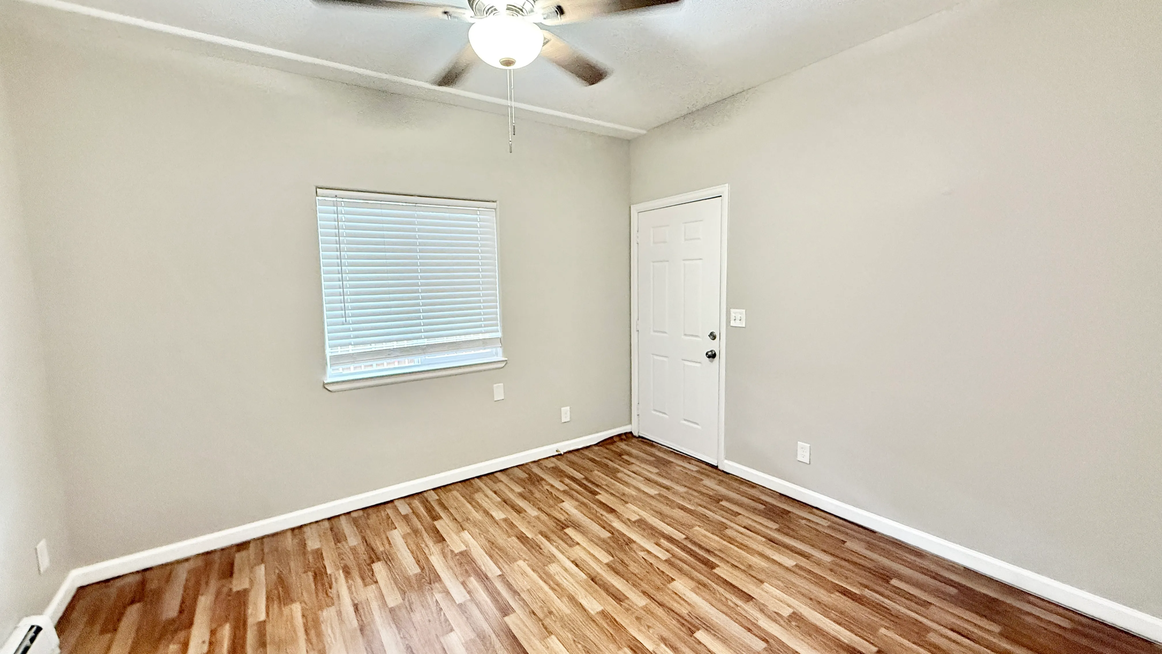 Inviting room with elegant hardwood flooring, a ceiling fan, and ample natural light through the window.