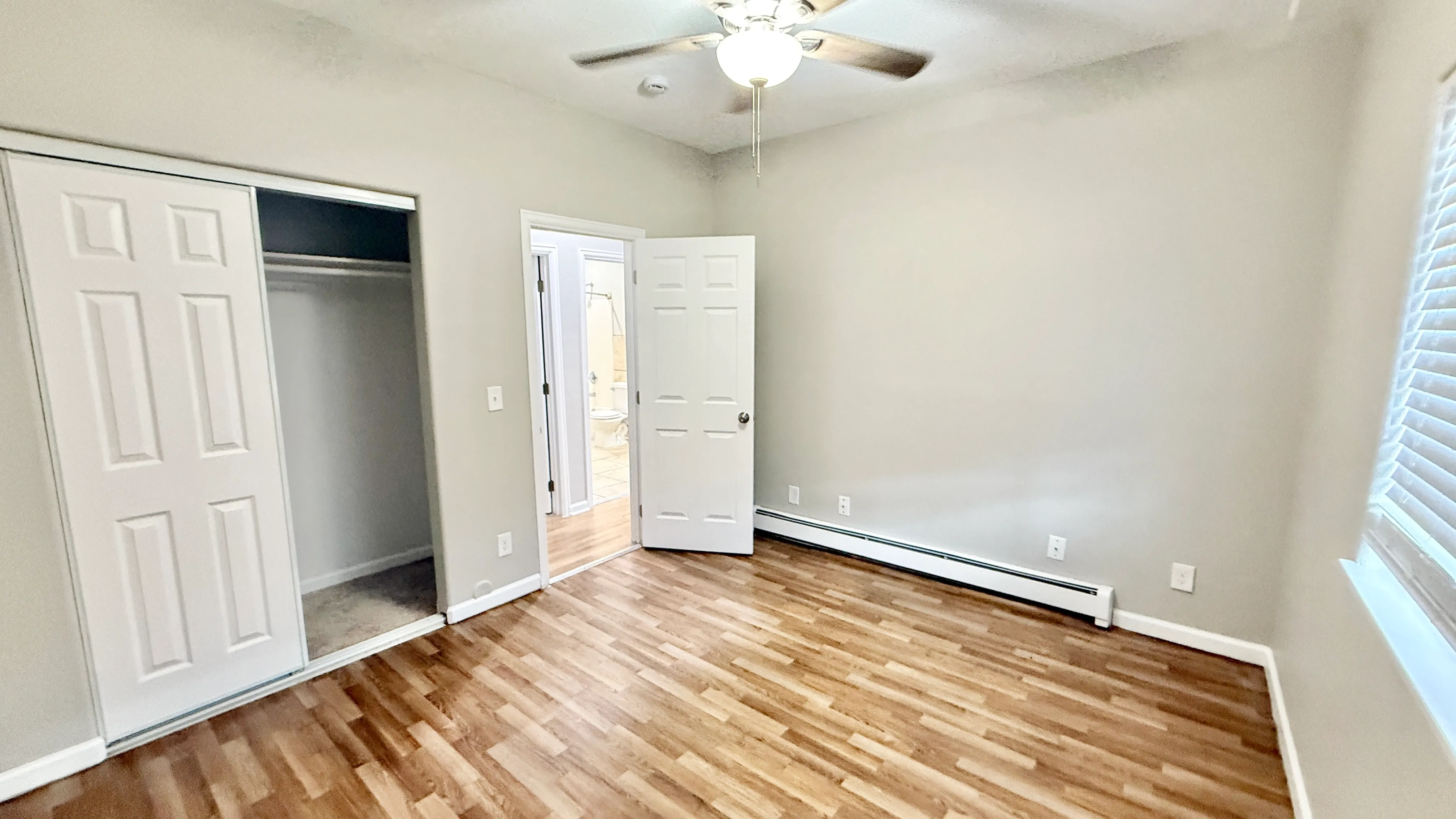 Bright and airy bedroom with laminate flooring, closet space, and bathroom access in a modern apartment.