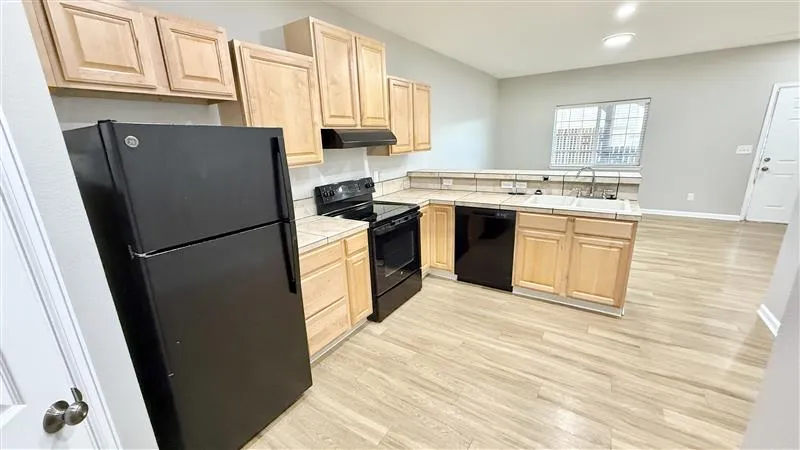 Modern kitchen with light wood cabinets, sleek black appliances, and spacious open layout.