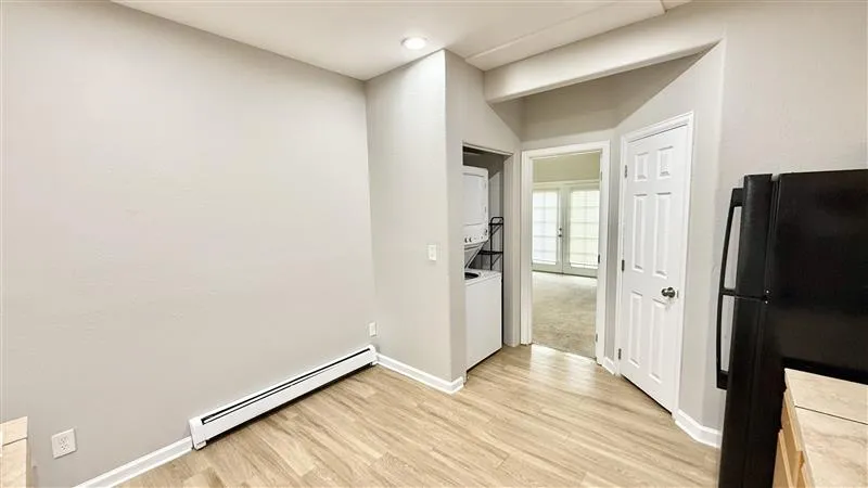 Bright and inviting apartment corner featuring modern wood flooring, in-unit laundry, and a glimpse into a sunlit room.