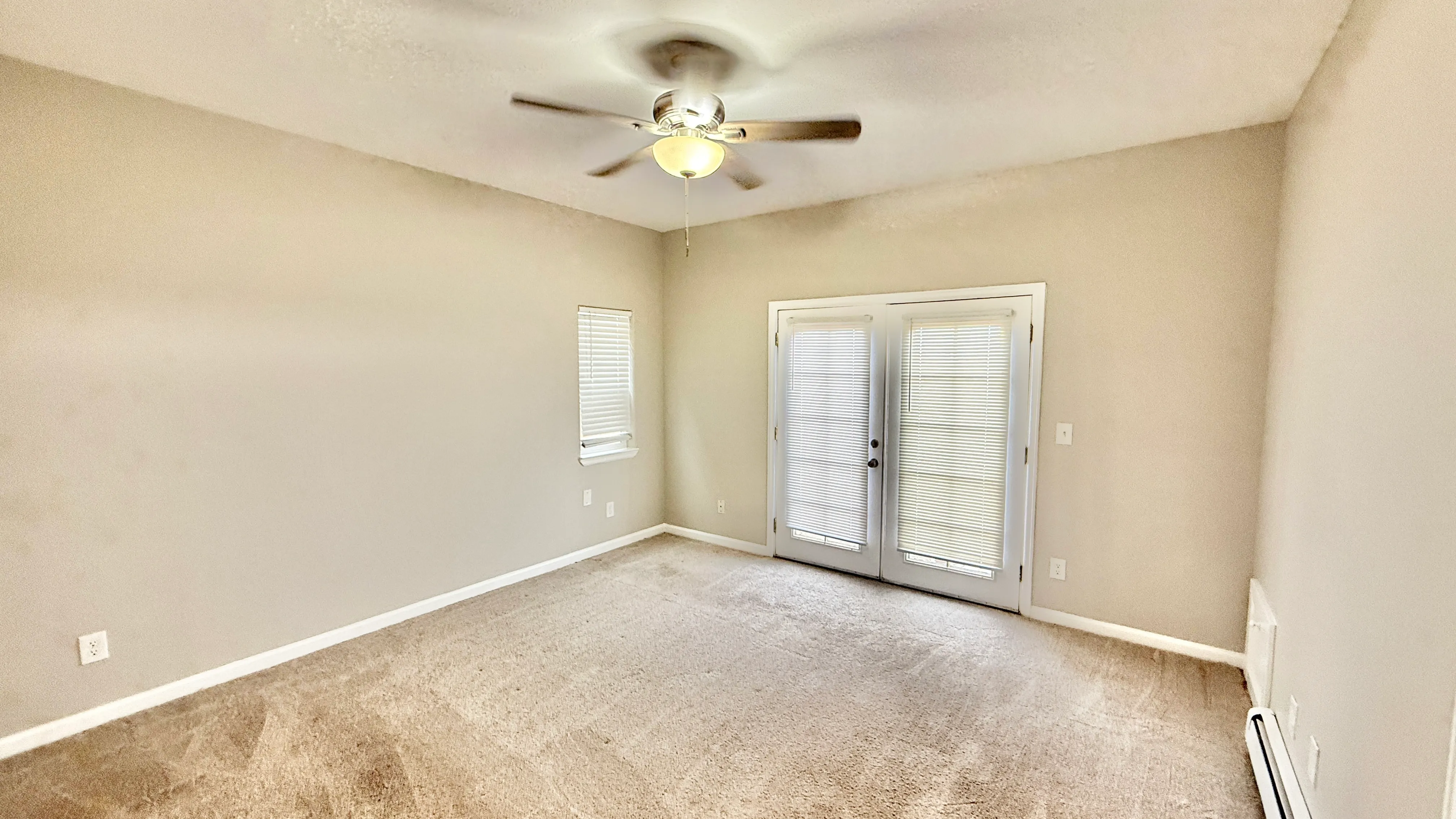Bright and spacious bedroom with neutral carpet, ceiling fan, and French doors leading to a patio.