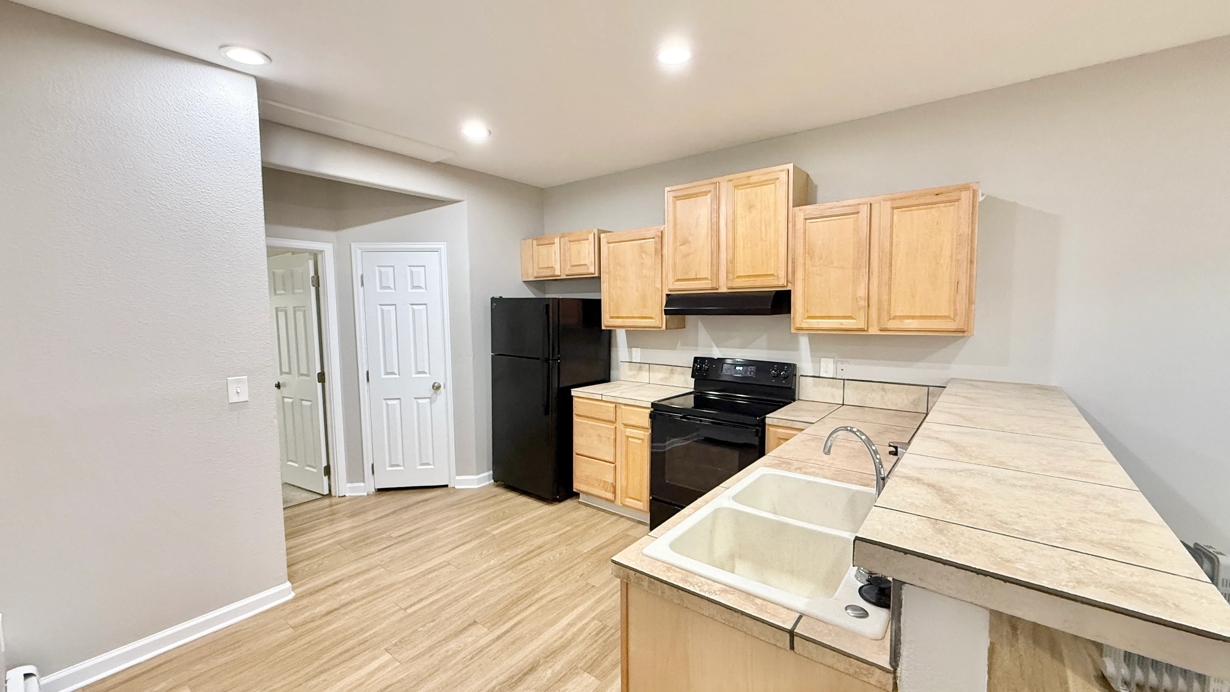 Modern kitchen with ample wooden cabinetry, sleek black appliances, and elegant tiled countertops.