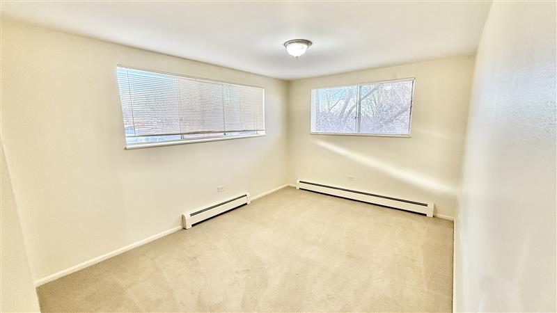 Bright and airy room with large windows, fresh white walls, and soft carpeting, perfect for a cozy bedroom or office space.