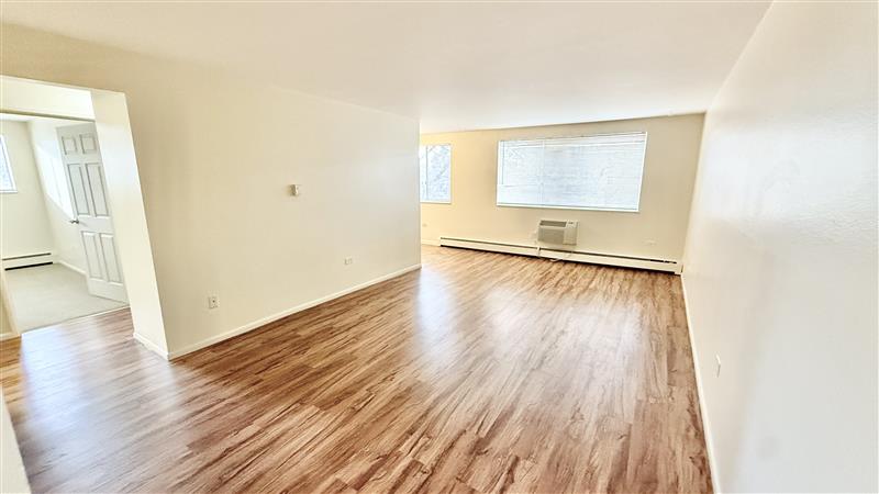 Bright and spacious living room with sleek wooden flooring and large windows, offering ample natural light.