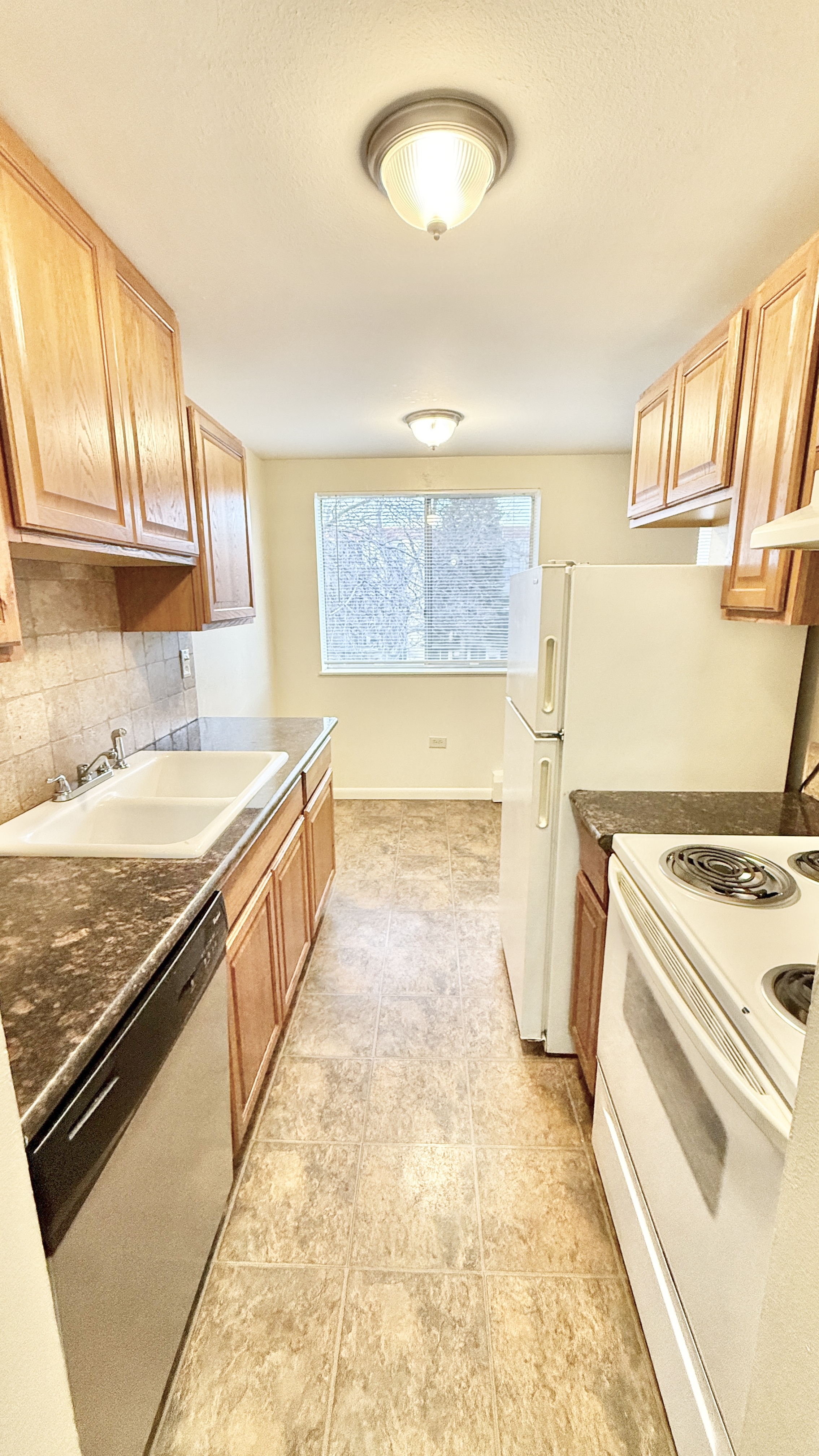 Bright and inviting galley kitchen with modern appliances, wooden cabinetry, and elegant stone countertops, featuring a large window with a peaceful view.