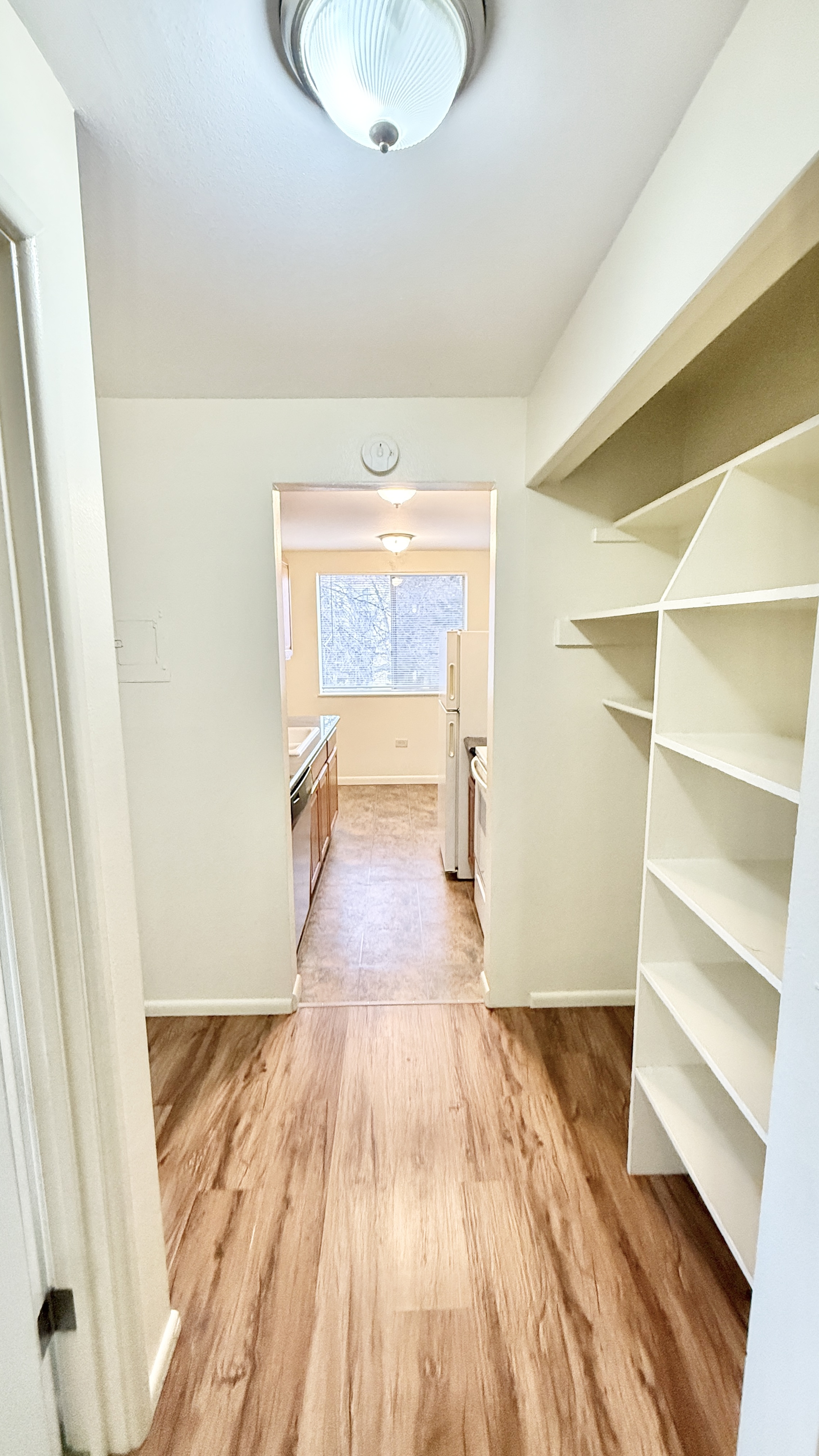 Charming hallway with elegant wooden flooring leading to a bright, spacious kitchen featuring modern appliances and ample shelving.