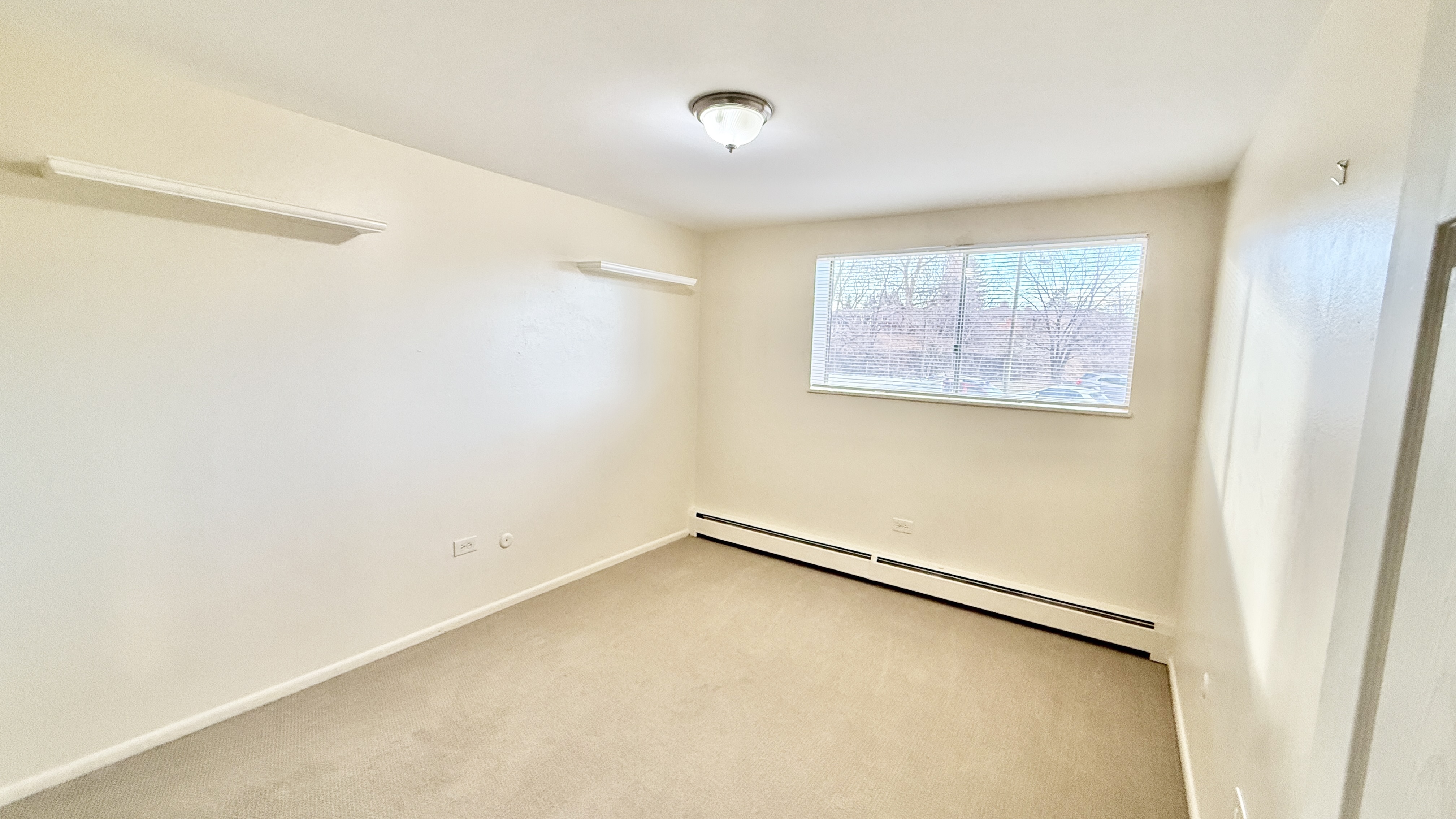 Bright, freshly painted room with large window offering natural light and cozy carpeting, perfect for a peaceful retreat.