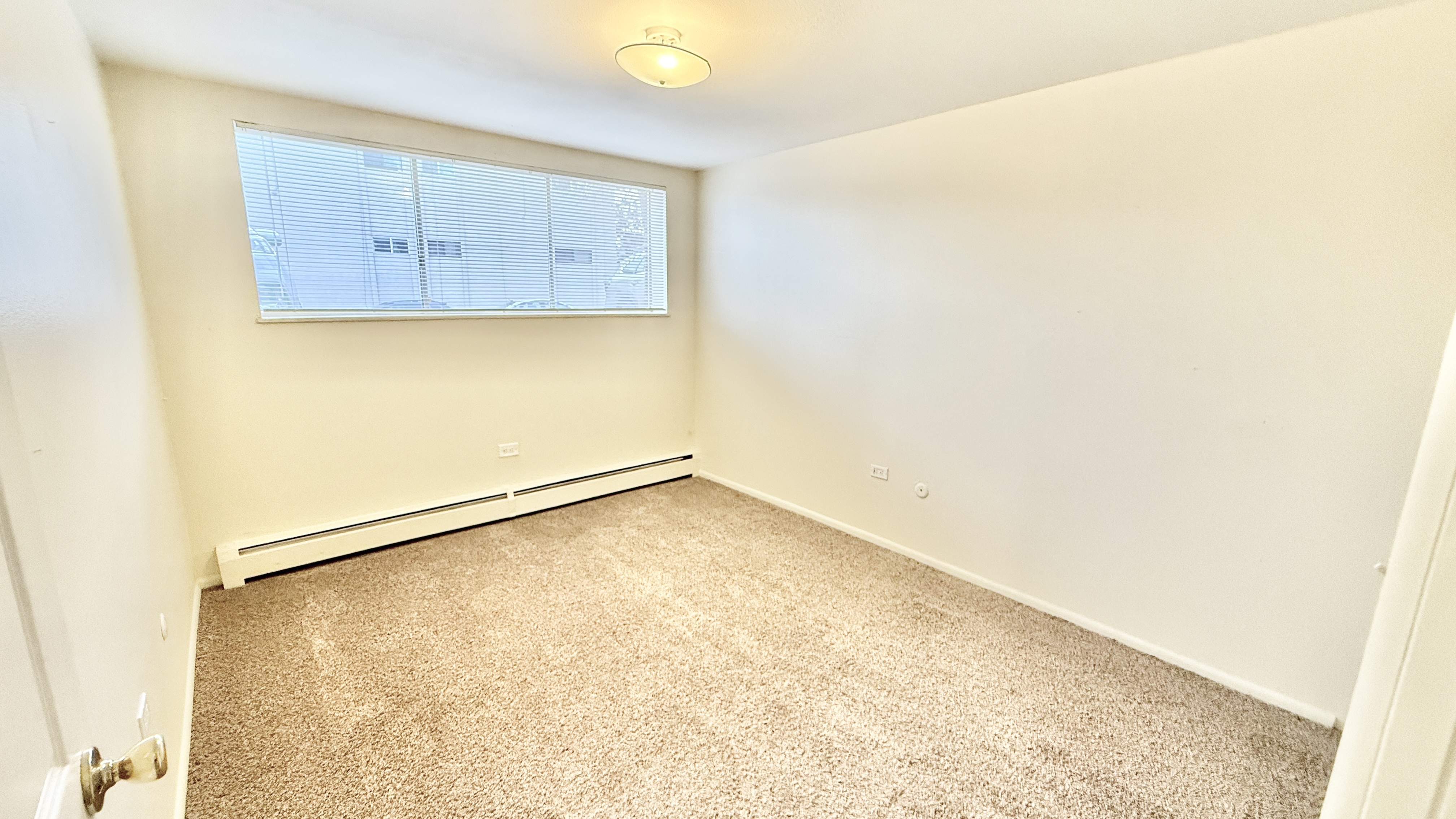 Bright and cozy empty room with plush carpeting, large window, and ceiling light fixture, ready for personalization.