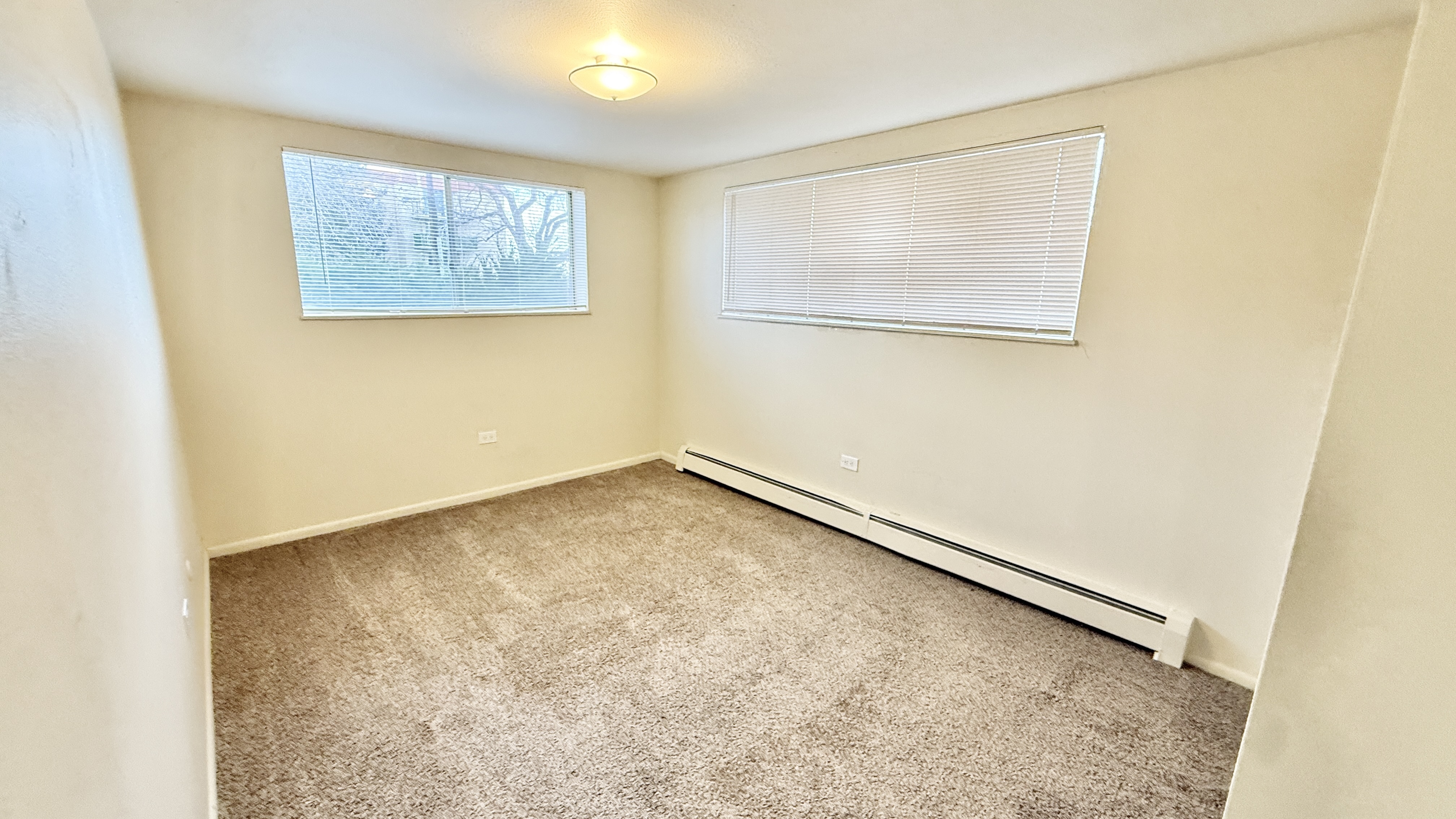 Bright and inviting room with large windows, neutral carpet, and soft lighting, perfect for personalizing.