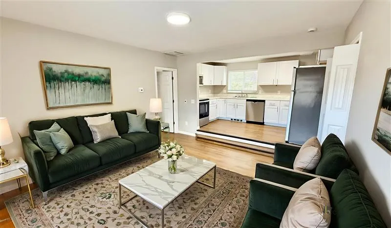 Inviting living room with elegant dark green sofas, chic coffee table, and open access to a modern, well-equipped kitchen.