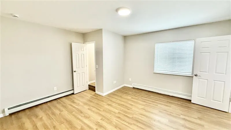 Bright and airy room with sleek wooden floors, modern white walls, and ample natural lighting from a large window with blinds.
