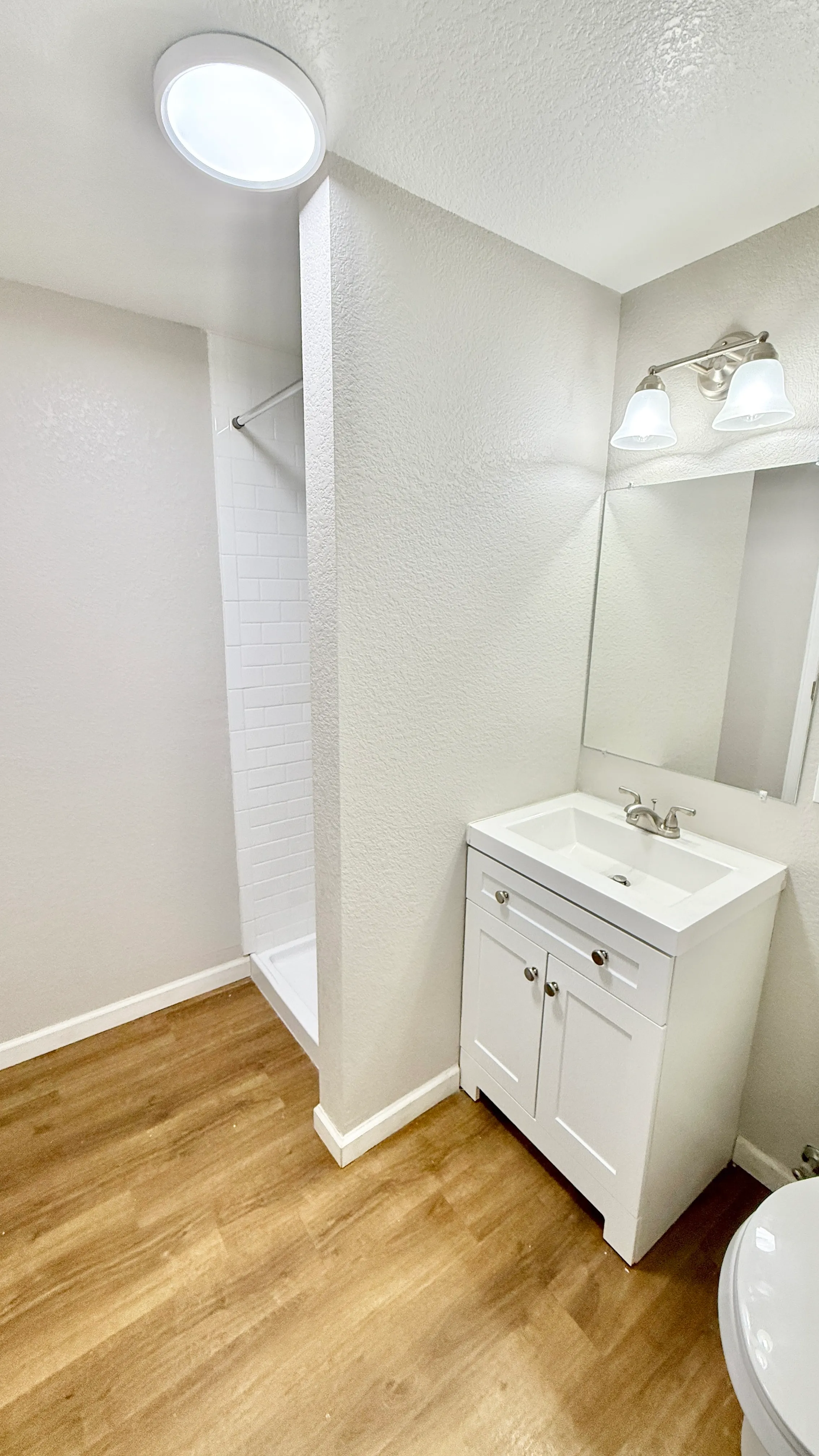 Sleek bathroom featuring modern white vanity, bright lighting, and wooden flooring for a stylish touch.