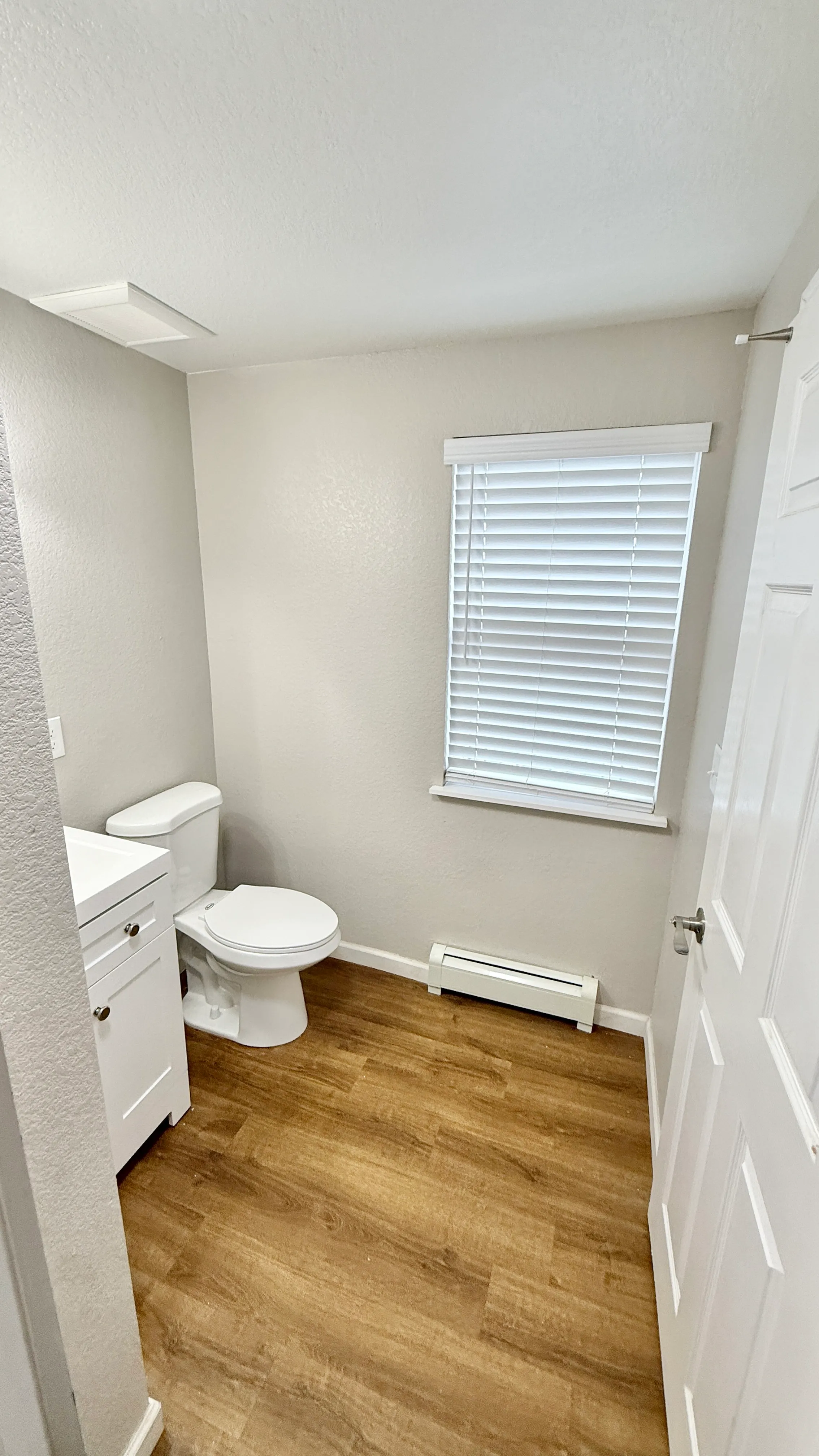 Bright and modern bathroom featuring sleek white fixtures and warm wood-style flooring.