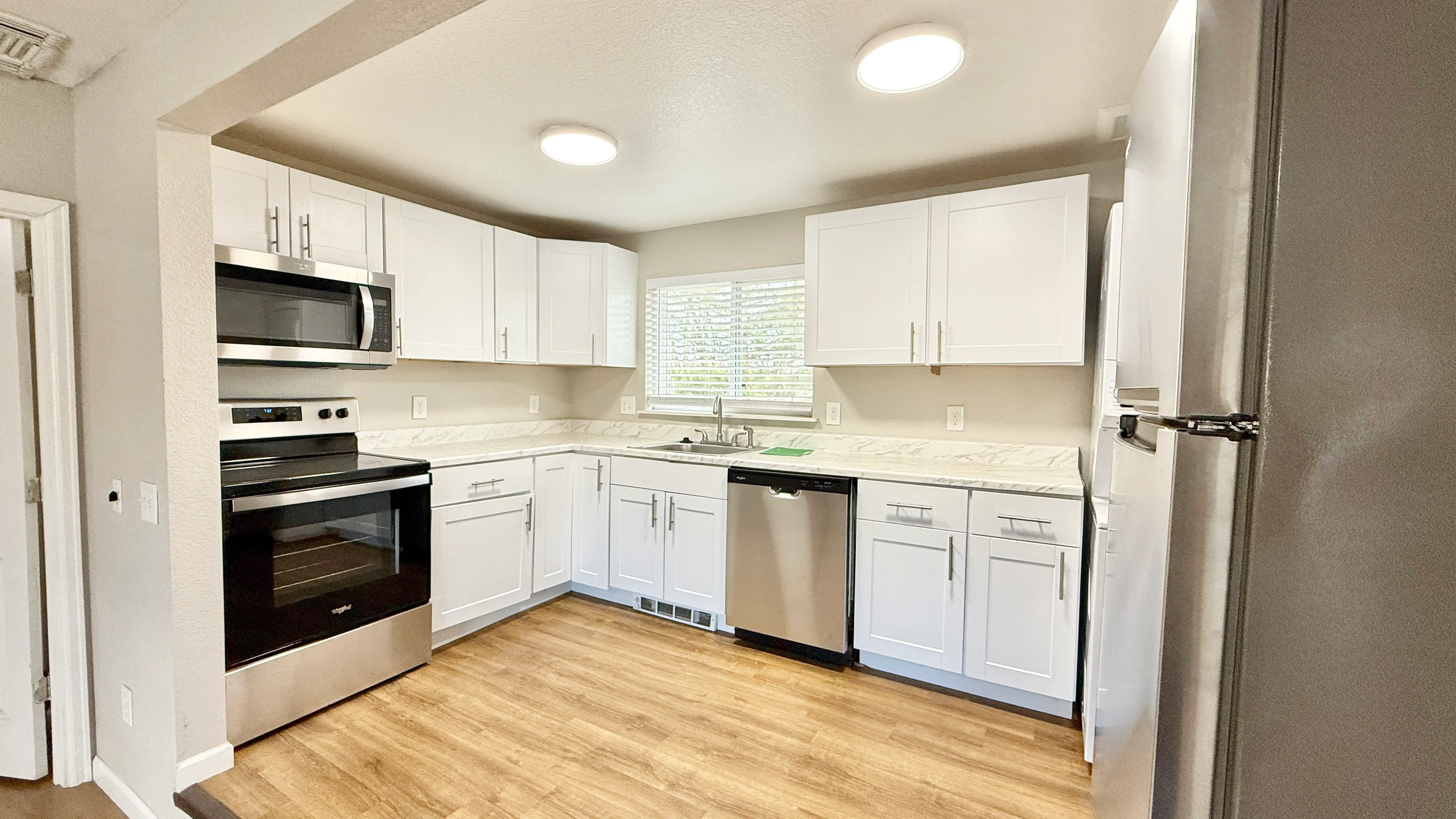 Modern kitchen with sleek stainless steel appliances, elegant white cabinets, and stylish wood flooring, offering a spacious and inviting cooking area.