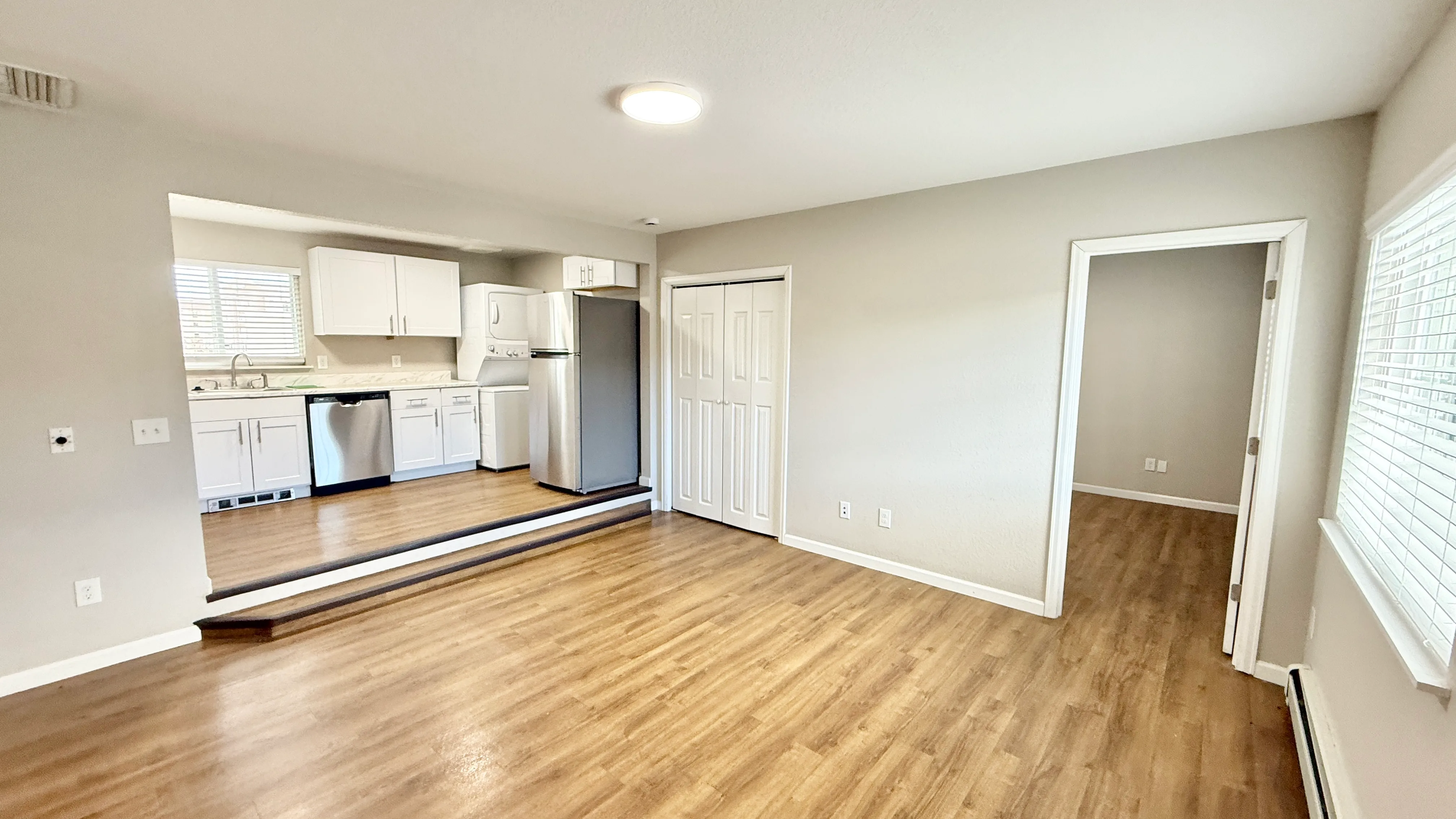 Bright open-concept living area with modern kitchen, featuring white cabinets, stainless steel appliances, and sleek hardwood flooring.
