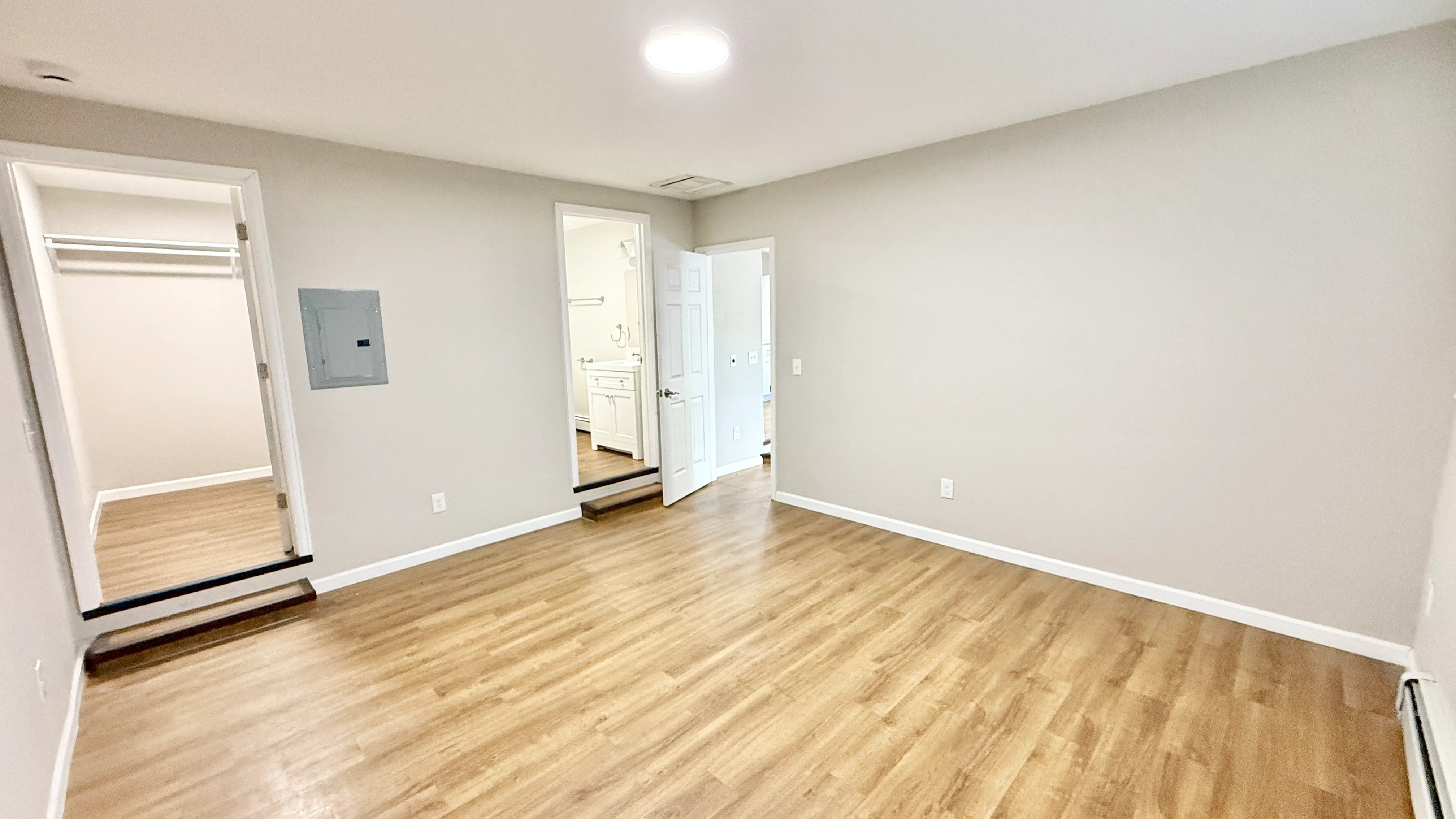 Bright and spacious room with modern wood flooring, fresh neutral paint, and an adjoining walk-in closet and bathroom.