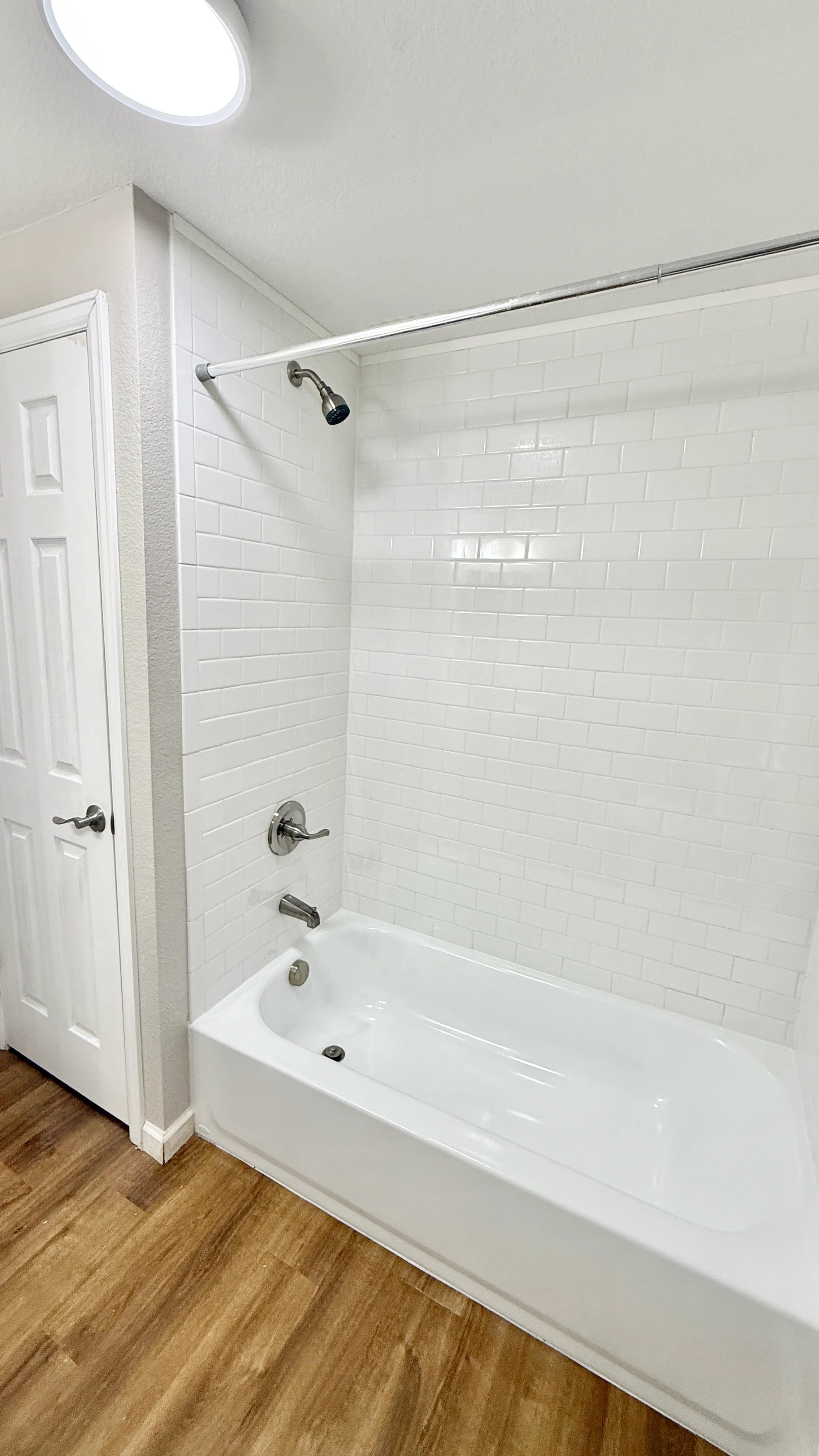 Modern bathroom featuring a sleek white bathtub and elegant wall tiles, accentuated by warm wood flooring.