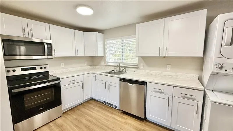 Modern kitchen with sleek stainless steel appliances, bright white cabinetry, and elegant marble countertops. Natural light fills the space, complementing the warm wood flooring.