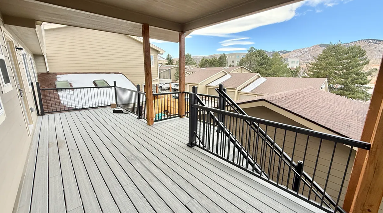 Spacious balcony with wooden decking, offering scenic views of rooftops and surrounding mountains.
