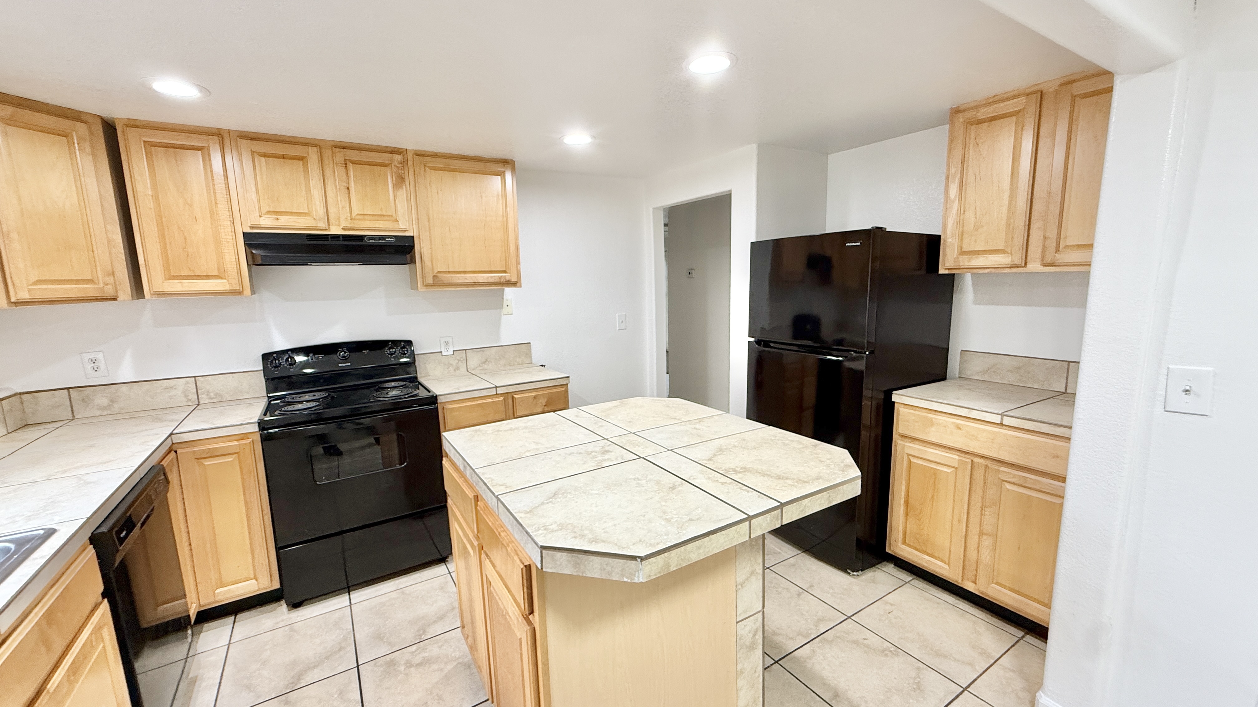 Modern kitchen with sleek black appliances, ample wooden cabinetry, and a spacious tiled countertop island.