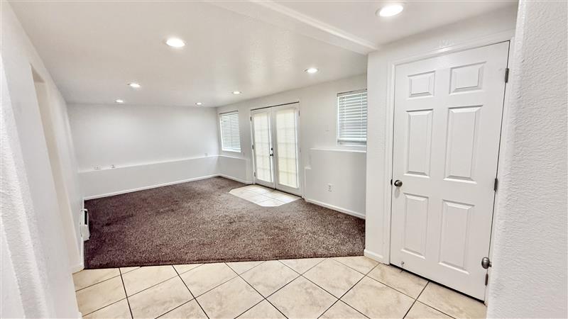 Bright and airy living space featuring modern recessed lighting, plush carpeting, and easy access to a tiled entryway.