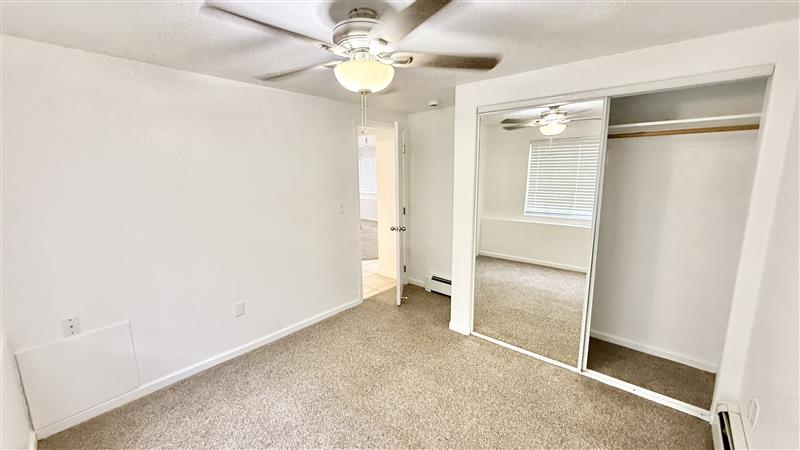 Inviting bedroom with plush carpet, mirrored closet doors, and ceiling fan for a cozy atmosphere.