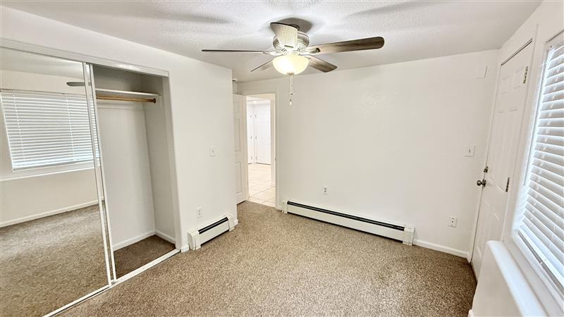 Bright and cozy bedroom with a ceiling fan, mirrored closet doors, and plush carpeted flooring.