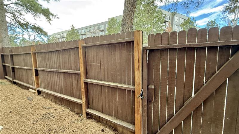 Charming wooden fence with natural surroundings, pine trees, and a glimpse of modern apartments in the background.