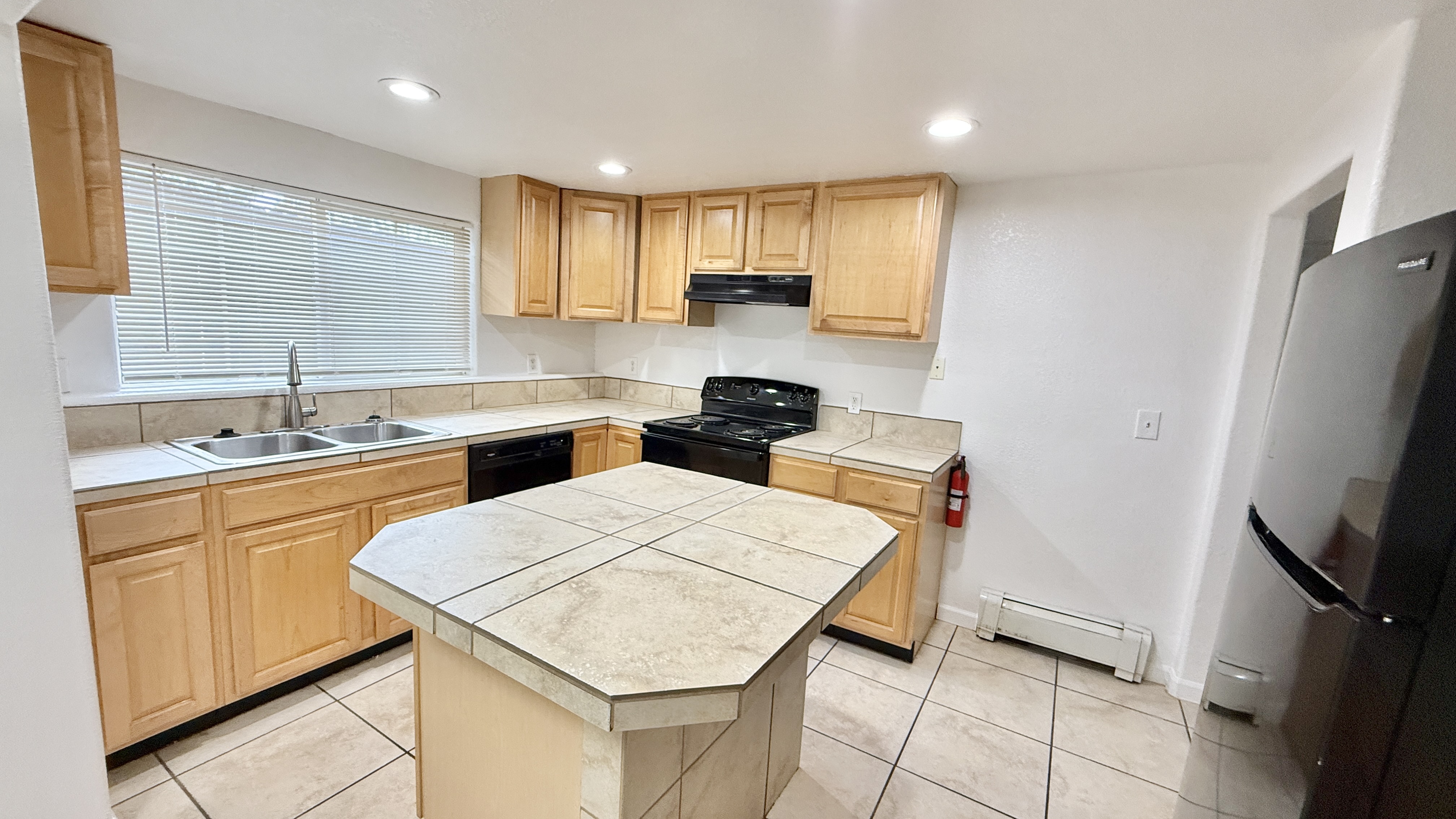 Modern kitchen with light wood cabinetry, island countertop, and sleek appliances illuminated by recessed lighting.