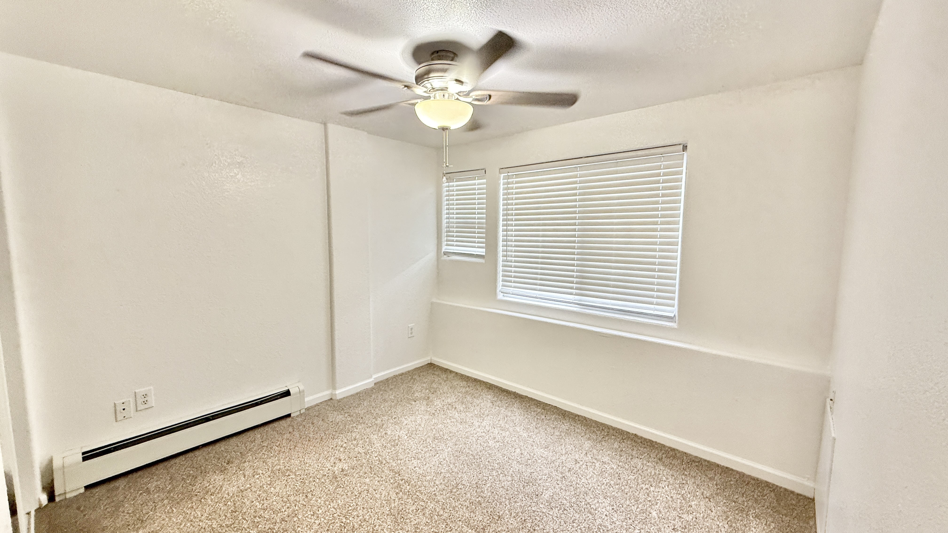 Bright, cozy room with neutral carpeting, large window with blinds, and ceiling fan, perfect for a relaxing retreat.