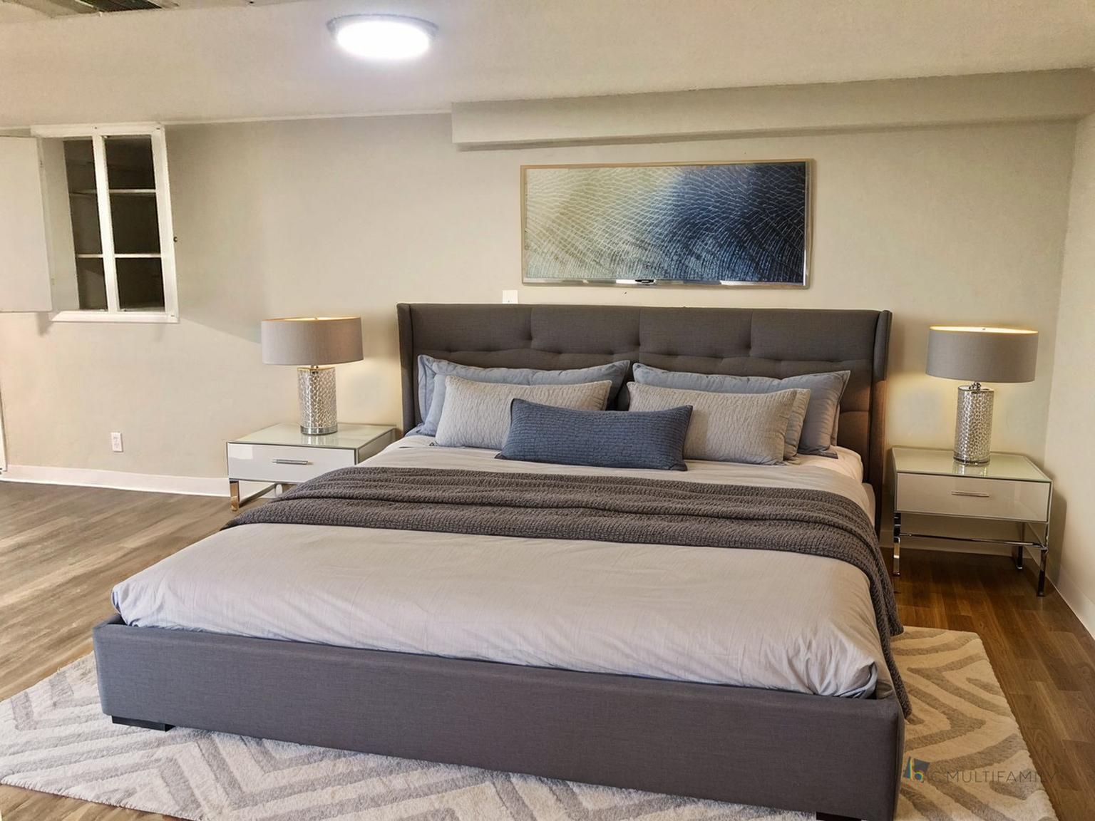 Elegant bedroom featuring a plush queen-sized bed with stylish cushions, sleek nightstands with modern lamps, and a chic abstract artwork above the bed.