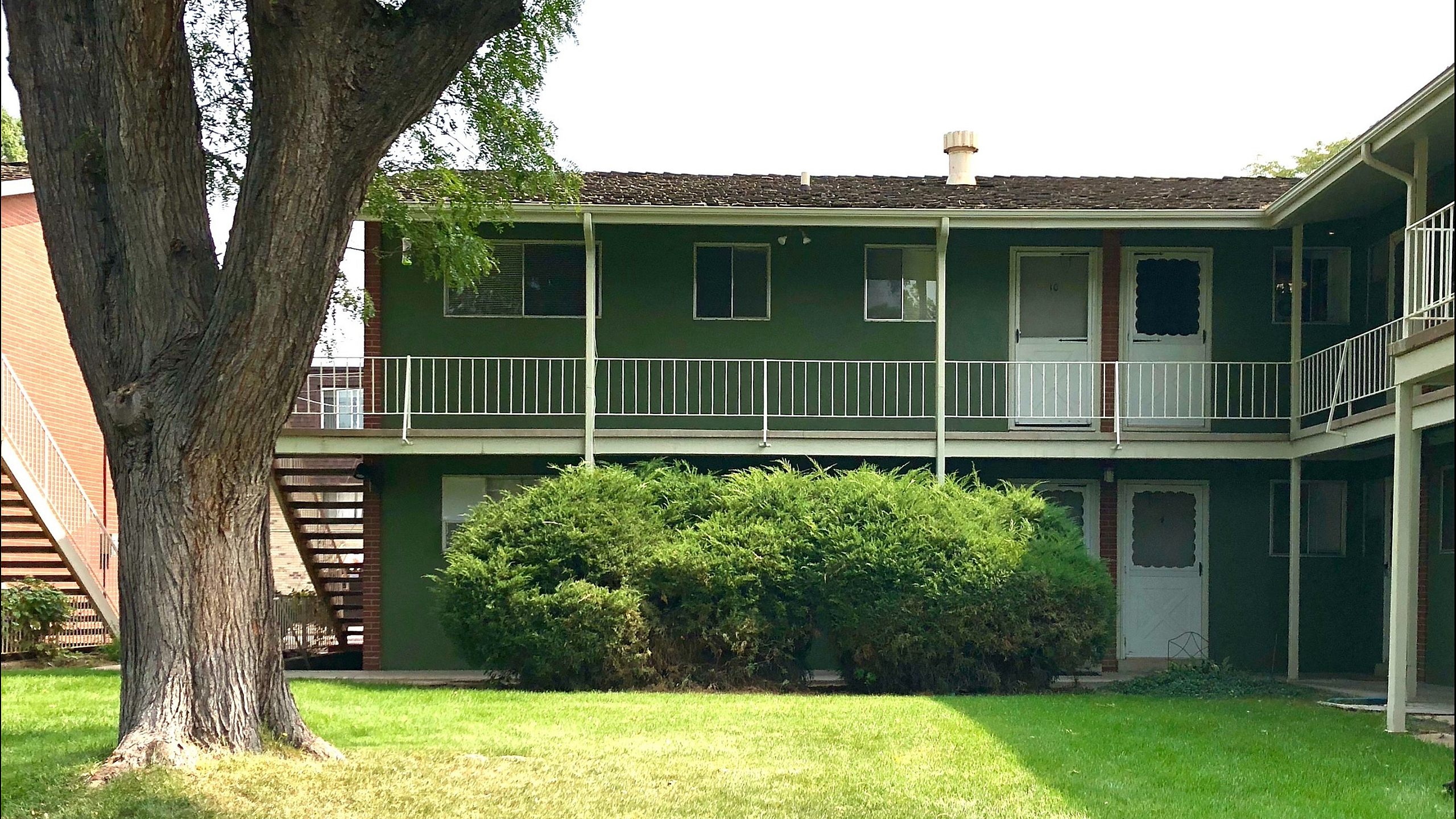 Inviting two-story apartment building with green exterior and white railings, surrounded by lush greenery.