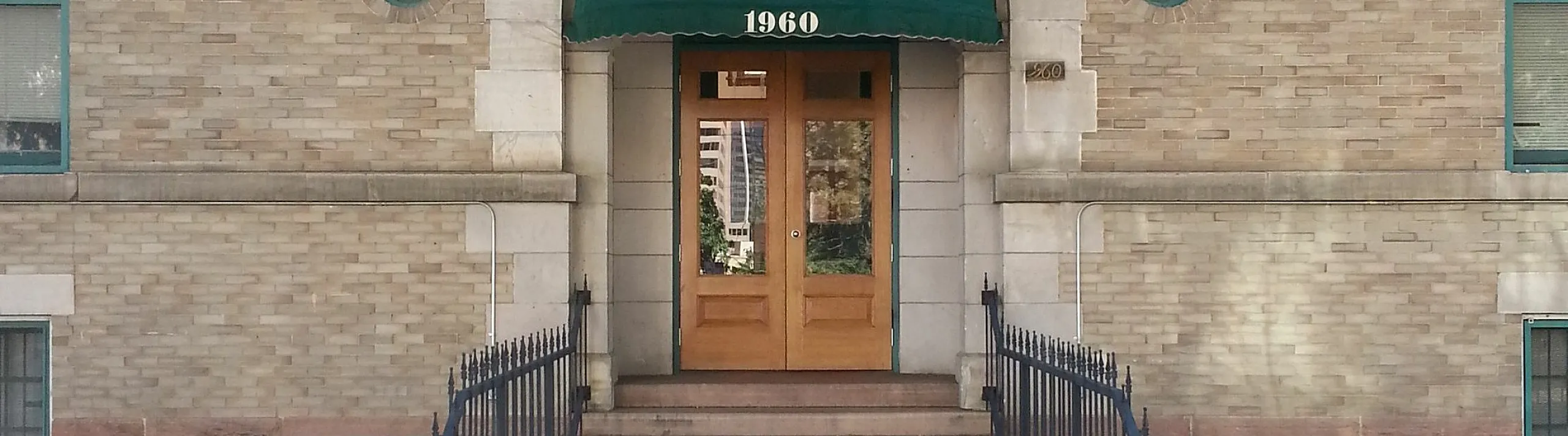 Charming brick apartment building with decorative archway and green awning at entrance.