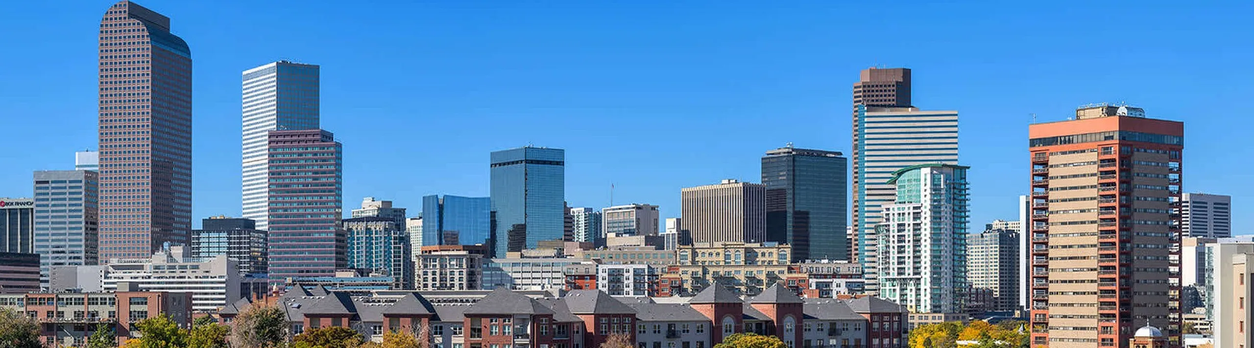 Panoramic view of a lively cityscape with modern skyscrapers and lush autumn trees.