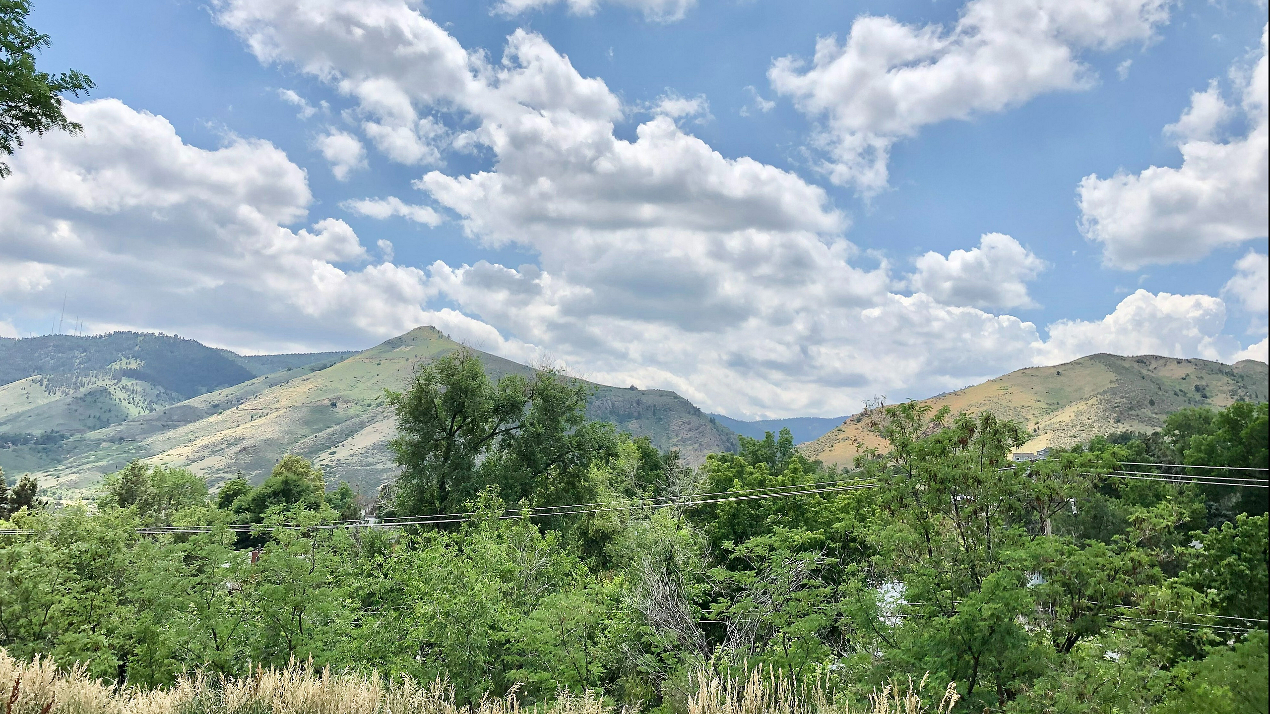 Breathtaking view of green mountains under a vibrant blue sky with fluffy clouds, seen from an apartment.