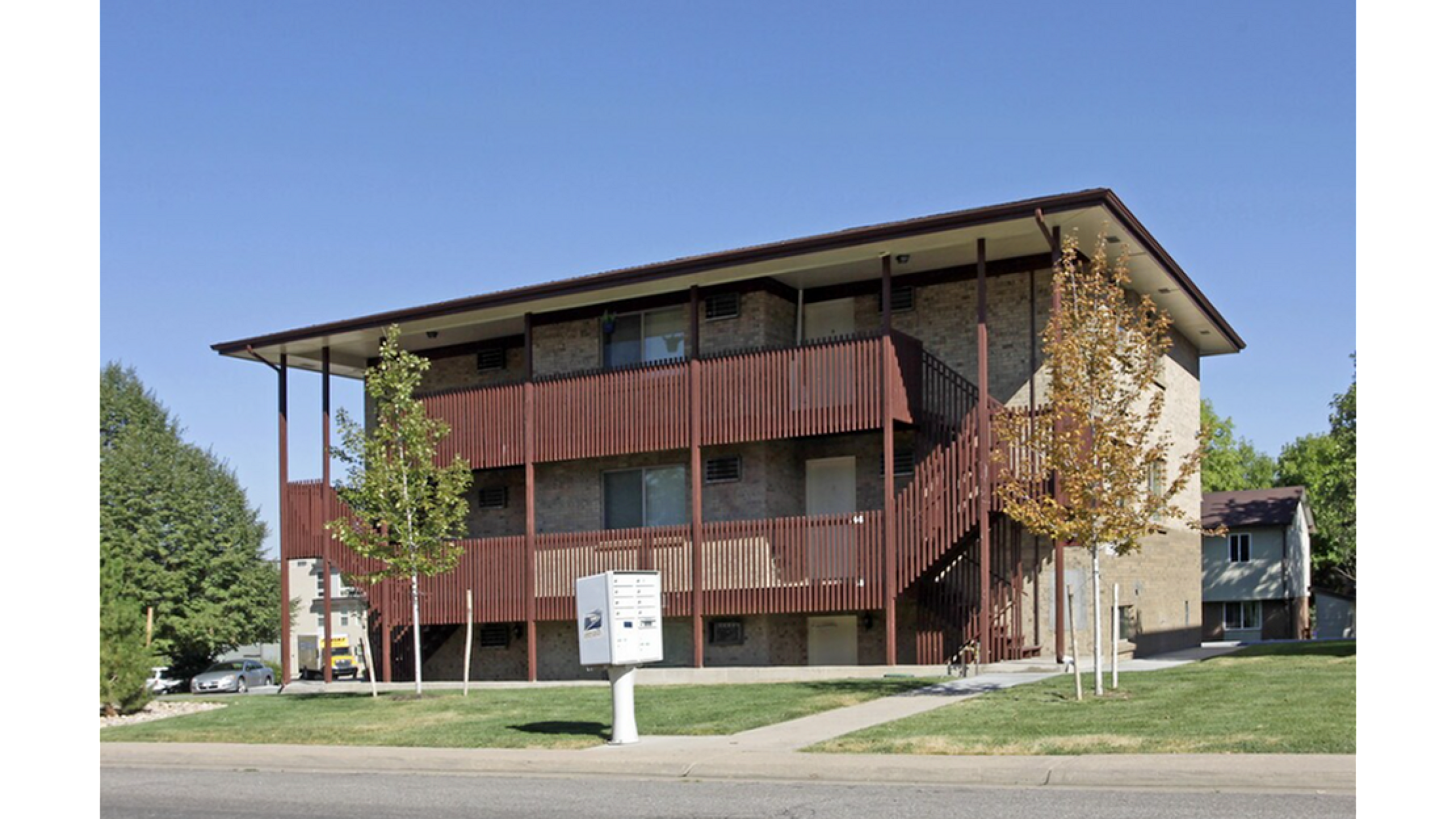 Three-story apartment building with a modern wood facade and surrounding green space.