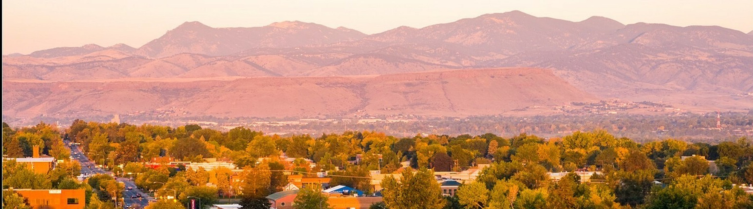Charming cityscape with vibrant trees and distant mountainous backdrop at sunset.