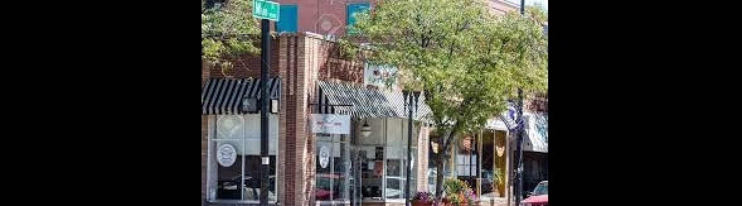 Scenic street view with brick storefronts, large windows, and lush green trees.