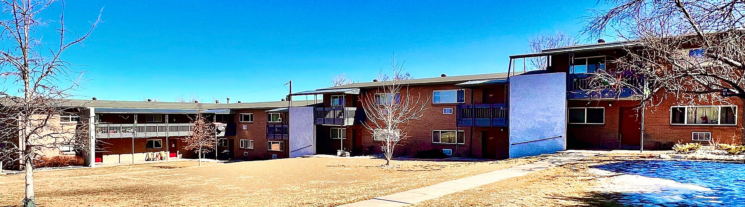 Charming apartment complex with green open space under a clear blue sky.