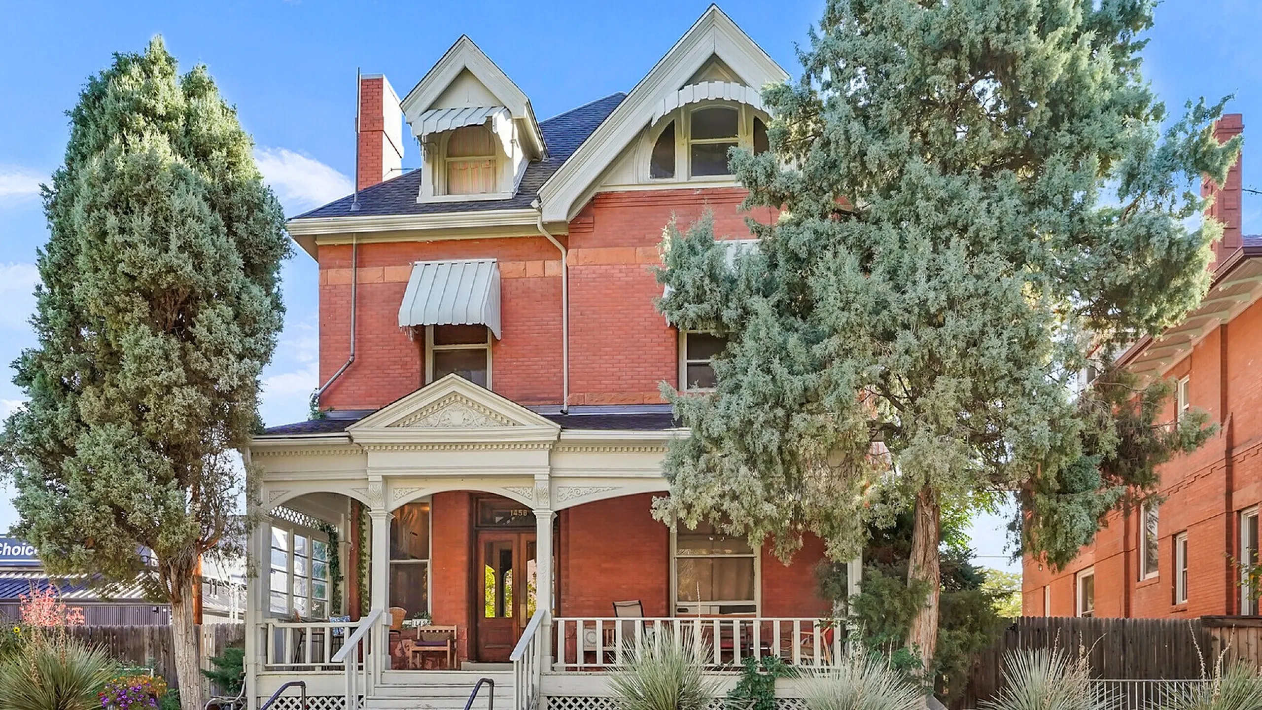 Stunning brick Victorian house with a large porch and lush greenery.