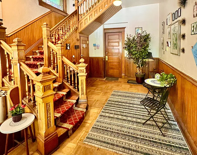 Inviting foyer with a grand wooden staircase, vibrant red carpet, and stylish decor.