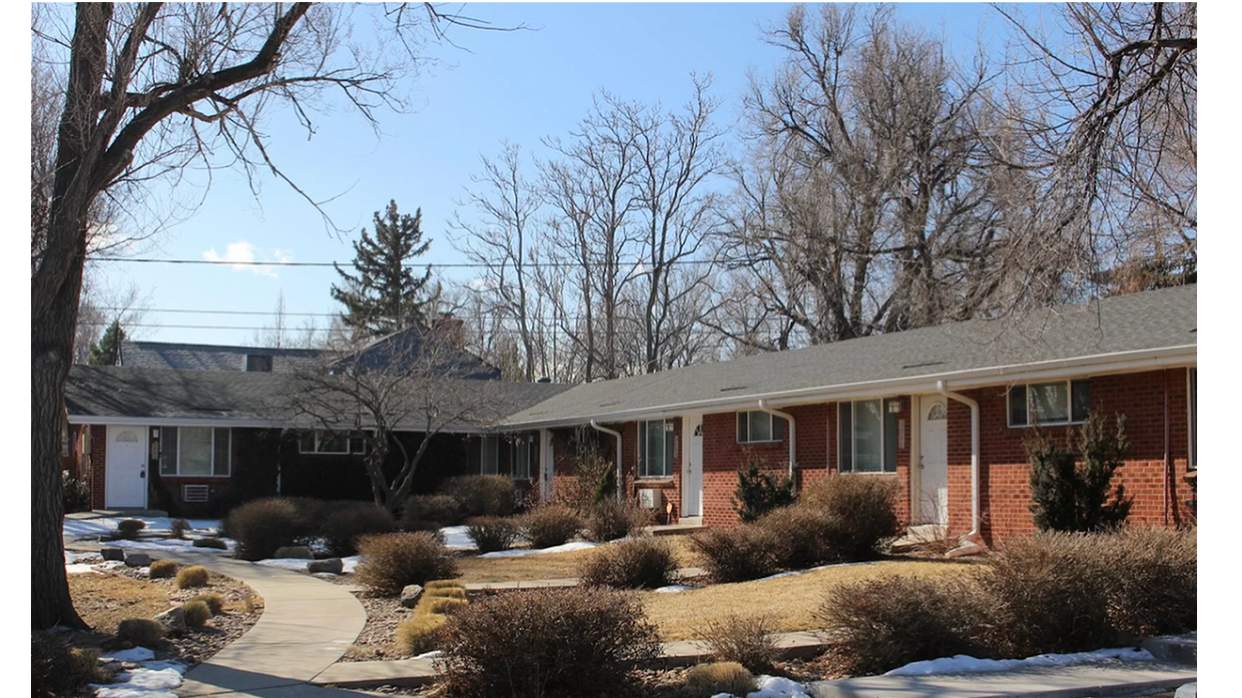 Charming brick apartment complex with snowy landscaping and clear blue sky.