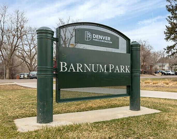 Entrance sign for Barnum Park in Denver, featuring lush greenery and a clear blue sky.