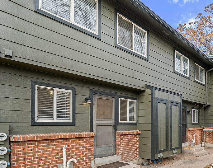 Charming duplex with green siding and brick accents, featuring steps leading to each entry with a small patio area.