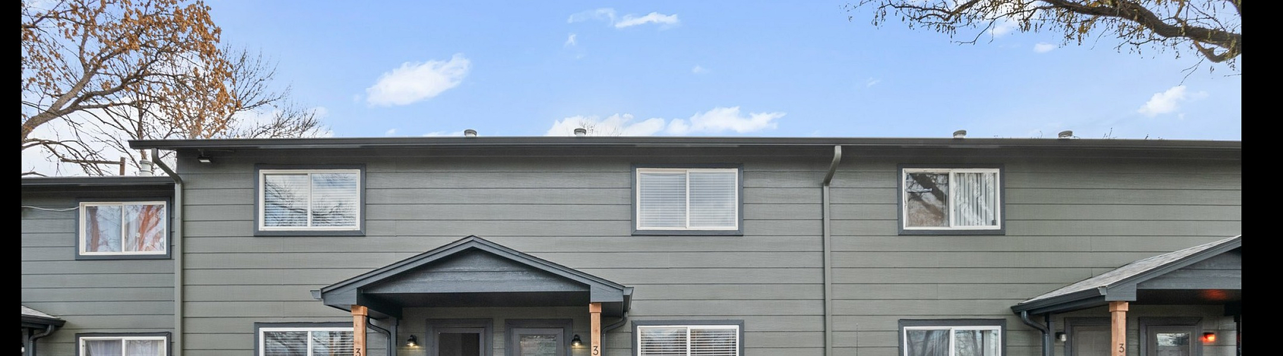 Modern two-story apartment with green siding and brick accents, featuring a welcoming entrance and ample parking space.